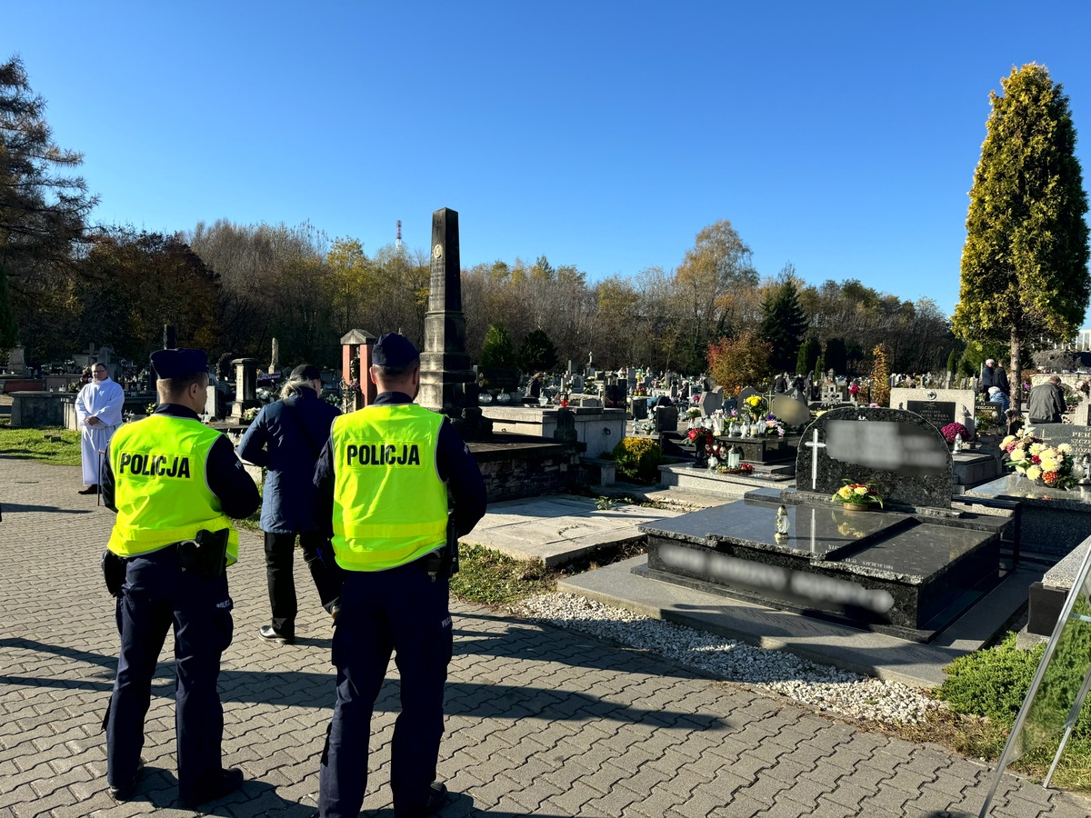 Umundurowani policjanci w odblaskowych kamizelkach strzegacy porzadku na cmentarzu.