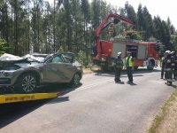 zniszczony samochód na lawecie, w tle policjanci i strażacy