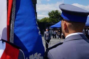 Policjant ze sztandarem, w tle dowódca uroczystości