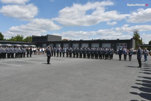 Dowódca uroczystości stojący na środku placu wewnętrznego komendy.  Wokół niego stojący w szeregach policjanci.