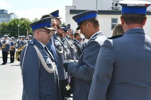 Przedstawiciele policyjnych związków zawodowych wręczają stojącym w rzędzie policjantom medale związkowe i składają gratulacje.