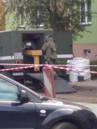 Patrol sapersko-minerski , wchodzący do pojazdu ubrany w sprzęt specjalistyczny żołnierz, na tle bloku.