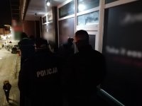 Jeden policjant umundurowany wraz z trzema policjantami operacyjnymi przed wejściem do lokalu.