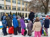 Grupa dzieci wraz z umundurowanym policjantem stojącym przed oznakowanym radiowozem