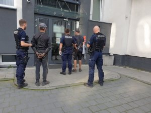 Trzech umundurowanych policjantów doprowadzających do komendy dwóch zatrzymanych mężczyzn