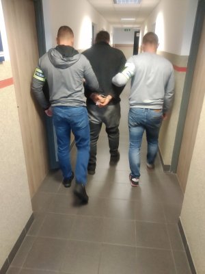 Nieumundurowani policjanci prowadzą zatrzymanego mężczyznę