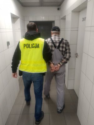 Policjant prowadzący zatrzymanego mężczyznę korytarzem aresztu