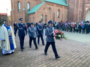 Zdjęcia przedstawiające czterech umundurowanych galowo Policjantów o raz księdza w szacie liturgicznej, którzy to idą w kierunku kolumbarium by złożyć wieniec w hołdzie poległym. W tle poczty sztandarowe i orkiestra górników.