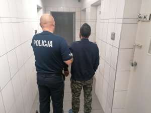 Zatrzymany prowadzony przez umundurowanego policjanta korytarzem aresztu policyjnego.