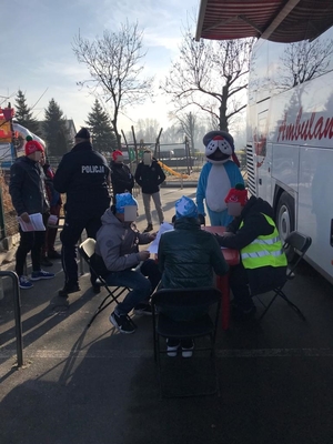 Umundurowany policjant oraz maskotka policyjna Sznupek nad zbiornikiem wodnym Pogoria III, podczas spotkania z osobami morsującymi, oddajacymi krew oraz w trakcie wreczania odblasków turystom wypoczywającym zimą nad wodą.