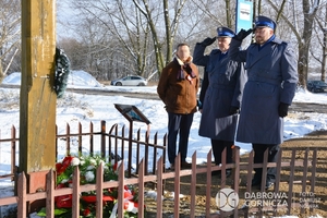 Na zdjęciu 2 umundurowanych policjantów składających hołd przed krzyżem . W tle stojący mężczyzna.