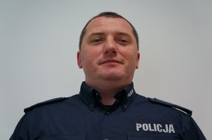 Wizerunek umundurowanego policjanta stojącego przodem do obiektywu.