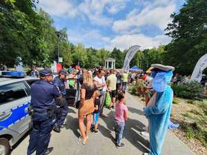 Umundurowani Policjanci i maskotka policyjna Sznupek , radiowóz oznakowany i motocykl służbowy w trakcie trwania 2 Dziecięcego Festiwalu Biegowego.