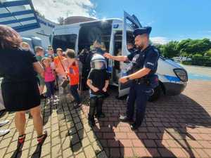 Umundurowani policjanci w trakcie spotkania z młodzieżą na dąbrowskich basenach, prezentujący stoisko policyjne oraz sprzęt policyjny.
