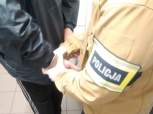 Nieumundurowany policjant z opaską z napisem POLICJA na lewy ramieniu.