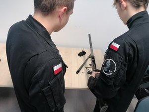 Uczniowie Klasy mundurowej podczas wizyty w komendzie policji na zajęciach prowadzonych przez umundurowanych policjantów.