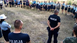 Umundurowani policjanci , strażacy i harcerze podczas sprawdzania obozowiska usytuowanego w lesie.