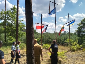 Umundurowani policjanci , strażacy i harcerze podczas sprawdzania obozowiska usytuowanego w lesie.