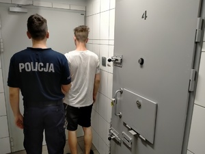 Umundurowany policjant z zatrzymanym stojący obok celi policyjnej.