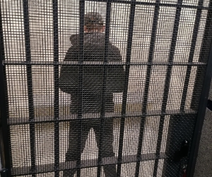 Zatrzymany mężczyzna stojący tyłem za kratami drzwi do celi policyjnej.