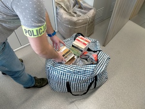 podrobione perfumy i ubrania zliczane przez nieumundurowanego policjanta z opaska na ramieniu z napisem policja.
