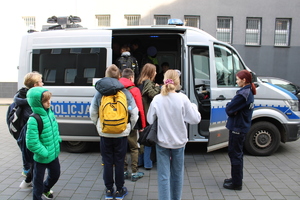 Umundurowani policjanci na zdjęciu z dziećmi oglądającymi oznakowany radiowóz policyjny.