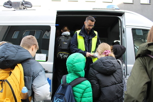 Umundurowani policjanci na zdjęciu z dziećmi oglądającymi oznakowany radiowóz policyjny.