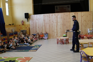 umundurowany policjant prowadzący pogadankę dla dzieci. dzieci siedzą na podłodze naprzeciwko policjanta.