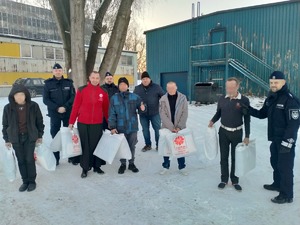 Umundurowani policjanci i ksiądz wraz z pracownikami Caritas pozują do zdjęcia. Na zdjęciu widzimy uniesione kciuki do góry osób które zostały obdarowane pakietami.