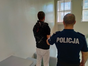 Na zdjęciu widzimy umundurowanego policjanta stojącego z zatrzymanym w celi policyjnej - tyłem.