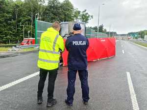 Na zdjęciu widzimy umundurowanych strażaków i policjantów oraz oznakowane radiowozy tych służb podczas działań na drodze ekspresowej.