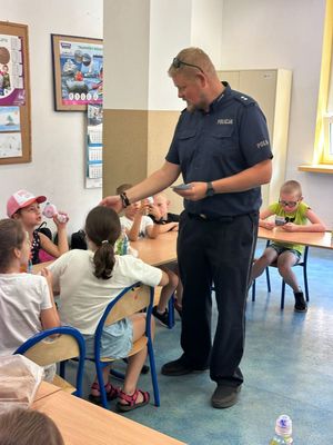 Na zdjęciu widzimy umundurowanego policjanta prowadzącego prelekcje w miejscach wypoczynku dzieci i młodzieży na trenie Dąbrowy Górniczej.