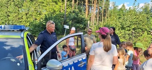 Na zdjęciu widzimy umundurowanych policjantów i strażników leśnych w trakcie działań na terenach zielonych. Mundurowi przeprowadzają rozmowy z wypoczywającymi na łonie natury.