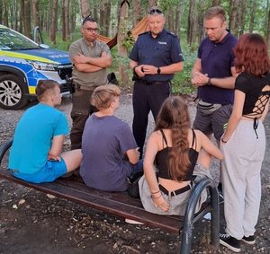 Na zdjęciu widzimy umundurowanych policjantów i strażników leśnych w trakcie działań na terenach zielonych. Mundurowi przeprowadzają rozmowy z wypoczywającymi na łonie natury.