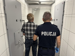 Umundurowany policjant z zatrzymanym w pomieszczeniu dla osób zatrzymanych.