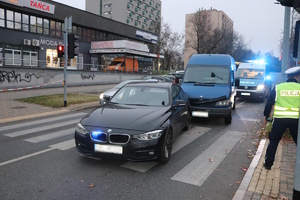 Na zdjęciu widać nieoznakowany radiowóz policyjny stojący przed samochodem dostawczym, za tymi pojazdami STOI OZNAKOWANY RADIOWÓZ. w PRAWEJ części zdjęcia WIDAĆ UMUNDUROWANEGO POLICJANTA stojącego TYŁEM W KAMIZELCE ODBLASKOWEJ.