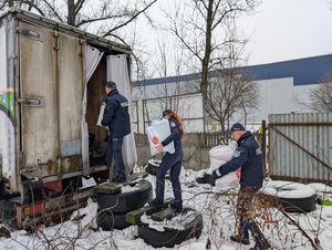 Umundurowani policjanci i pracownicy Caritas wraz z księdzem podczas rozdawani kocy, śpiworów dla bezdomnych.