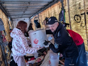 Umundurowani policjanci i pracownicy Caritas wraz z księdzem podczas rozdawani kocy, śpiworów dla bezdomnych.