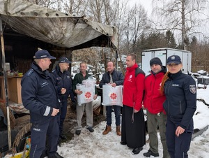 Umundurowani policjanci i pracownicy Caritas wraz z księdzem podczas rozdawani kocy, śpiworów dla bezdomnych.