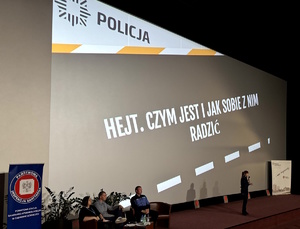 Umundurowani policjanci w trakcie debaty z młodzieżą w sali kinowej.