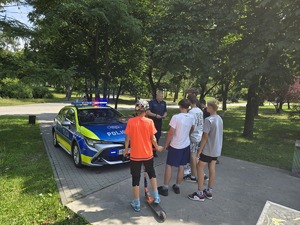 umundurowany policjant na tle radiowozu rozmawia z dziećmi.