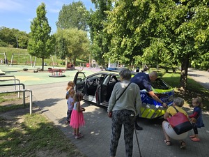 umundurowany policjant na tle radiowozu rozmawia z dziećmi.