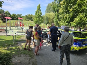 umundurowany policjant na tle radiowozu rozmawia z dziećmi.