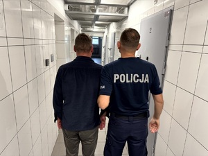 Odzyskana miedź i umundurowany policjant stojący tyłem z zatrzymanym w policyjnym areszcie