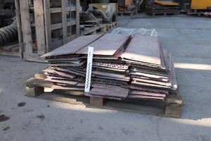 Odzyskana miedź i umundurowany policjant stojący tyłem z zatrzymanym w policyjnym areszcie