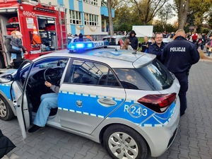 Umundurowani policjanci, radiowóz policyjny i maskotka Sznupek na festynie w przedszkolu.