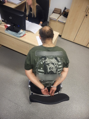 Widzimy policjantkę wykonującą czynności służbowe oraz mężczyznę z kajdankami założonymi na ręce trzymane z tyłu