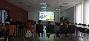 dzieci oglądają film profilaktyczny, po lewej stronie przy stole siedzi osoba