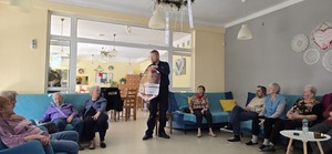 Widzimy Policjanta prowadzącego spotkanie i uczestniczących seniorów