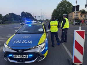Zdjęcie przedstawia radiowóz policyjny wraz z umundurowanymi policjantami podczas zabezpieczenia I Maratonu Zagłębiowskiego w dniu 23 maja 2026 roku.